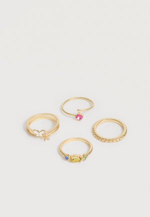 Vier goldene Ringe auf einer weißen Oberfläche angeordnet, davon einer mit einem Schmetterling, einer offen mit einem rosa Stein, einer mit einem gelben Stein, der von blauen und grünen Steinen flankiert ist, und einer mit einem strukturierten Band.