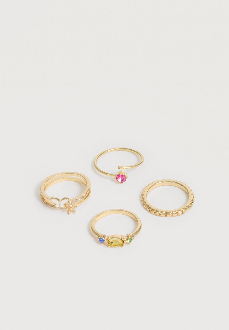 Τέσσερα χρυσά δαχτυλίδια τοποθετημένα σε λευκή επιφάνεια, με ένα με πεταλούδα, ένα ανοιχτό με ροζ πέτρα, ένα με κίτρινη πέτρα πλαισιωμένη από μπλε και πράσινες πέτρες, και ένα με υφασμένη μπάντα.
