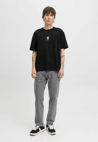 Sort bomulds t-shirt med et lille grafisk motiv på brystet, parret med grå jeans og sorte sneakers med hvide detaljer.