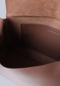Interieur van een bruin leren handtas met een gladde textuur, voorzien van een zijvak en subtiele branding. De voering is van lichtbruine suède.