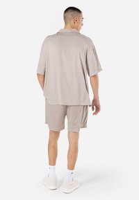 Lys beige kortærmet skjorte med en afslappet pasform, parret med lys beige mesh shorts. Båret med hvide sokker og afslappede sneakers.