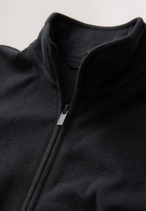 Čierna fleecová bunda s vysokým golierom, predným polovičným zipsom a jemným, textúrovaným povrchom. Disponuje minimalistickým dizajnom.