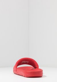 Sandalo rosso a scivolo con una parte superiore morbida e strutturata, dotata di un ampio cinturino e un plantare sagomato. La suola presenta un leggero motivo ondulato e un marchio.