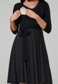 Vestido negro con mangas tres cuartos; cuerpo ajustado con escote en V; falda de lunares; lazos en la cintura; tela suave; diseño casual.