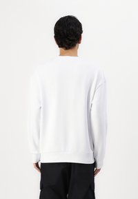 Hvit crewneck genser med avslappet passform, ribbede mansjetter og hem, laget av mykt stoff, uten synlige mønstre eller grafikk.