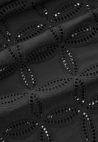 Tissu noir avec des motifs floraux découpés brodés, présentant des pétales en forme ovale avec de petits trous circulaires le long des bords.