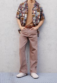 Chemise à manches courtes à motifs avec des couleurs marron, bleu et blanc ; t-shirt beige en dessous ; pantalon marron clair ; chaussures beige.