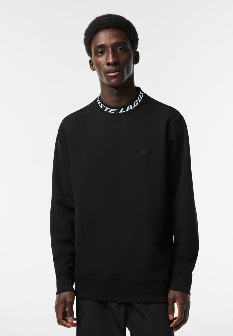 Zwarte sweatshirt van een katoenmix, met een ronde hals en een witte merkboord, lange mouwen en een klein logo op de borst.