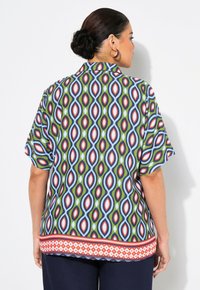 Kurzärmlige Bluse mit einem bunten geometrischen Muster aus roten, blauen, grünen und weißen Ovale. Ein kontrastierender Saum in Rot und Weiß.