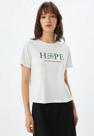 Hvid bomulds T-shirt med korte ærmer. Har "HOPE" i sort tekst og en grøn firkløver, med "LUCK FOR GOOD PEOPLE" nedenunder.