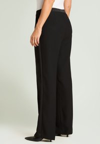 Pantalon noir à jambes larges avec une texture lisse, doté d'une taille haute et de coutures latérales avec un détail de bande contrastante.