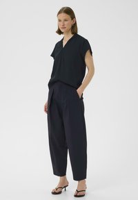 Top corto nero a maniche corte con scollo a V, abbinato a pantaloni blu navy a vita alta e larghi. Modello che indossa sandali piatti con lacci.