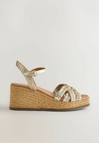 Sandale compensée métallique dorée avec motif tressé, bride cheville et semelle plateforme recouverte de jute.