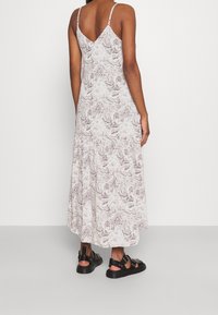 Robe longue sans manches à motifs en teintes claires avec un design marbré. Présente un dos en V et est accompagnée de sandales noires.