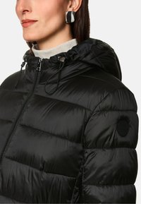 Schwarze gepolsterte Jacke mit Kapuze, ausgestattet mit einem Reißverschluss, Kordelzügen und einem runden Logo-Patch an der Schulter. Glatte, glänzende Stofftextur.