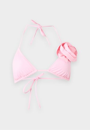 Młoda kobieta z długimi ciemnymi włosami w różowym bikini z detalem kwiatowym i teksturowanych czerwonych majtkach bikini, stojąca ze skrzyżowanymi ramionami.