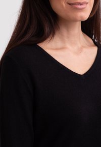 Sort v-hals sweater lavet af blødt stof, tætsiddende design, der viser en glat tekstur og subtile sy-detaljer langs halsudskæringen.