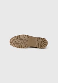 Suela de zapato marrón con surcos profundos y diseño de reloj con números romanos y manecillas de reloj grabados en la parte inferior.