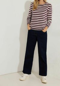 Gestreifter Pullover in Creme und Burgunder, kombiniert mit dunkelblauen weit geschnittenen Jeans. Das Model trägt weiße Sneaker und hat die Hände in den Taschen.