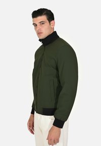 Giacca bomber verde oliva con colletto nero, chiusura a zip, polsini a coste e tasche laterali; texture liscia con design fitted.