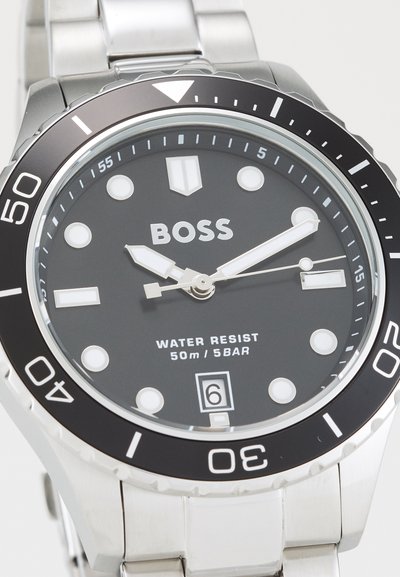 Montre en acier inoxydable avec un cadran noir, index horaires luminescents, lunette tournante et affichage de la date. Étanche jusqu'à 50 m.