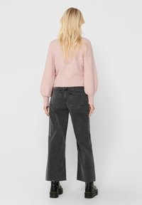 Rosa, texturerad tröja i kombination med mörkgrå, vida jeans. Ensemblet har en kort silhuett och en ribbad midja. Svarta stövlar fulländar looken.