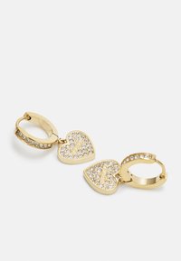 Boucles d'oreilles en or avec deux charms en forme de cœur ornés de cristaux transparents et estampillés du mot "GUESS."