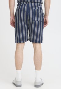 Námornícky modré pruhované šortky z textúrovaného materiálu s elastickým pásom a jedným zadným vreckom. Kombinované so sivými teniskami a bielymi ponožkami.