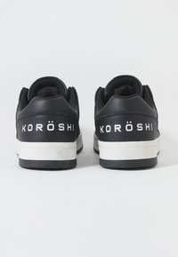 Sneakers negre din piele cu o talpă intermediară albă. Prezintă "KORÖSHI" în text alb pe călcâi. Formă rotunjită cu guler căptușit pentru confort.