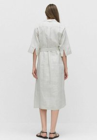 Jasnoszara sukienka z lnu z rękawami o średniej długości, przewiązywana w talii, z rozcięciami po bokach. Posiada kołnierz oraz prostą, luźną sylwetkę.