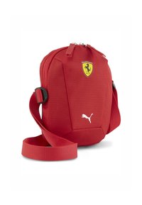 Geantă de umăr din material textil roșu, cu o suprafață texturată, având logo-ul Ferrari și logo-ul alb Puma, inclusiv o curea detașabilă și închidere cu fermoar.