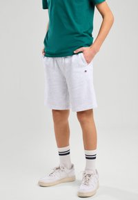 Shorts in cotone grigio con tasche laterali, cintura elastica e un piccolo logo. Abbinati a una t-shirt teal e sneakers bianche con strisce scure sui calzini.