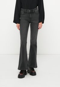 Platų juodų džinsų kelnės su aukštu juosmeniu, su subtiliomis dėvėjimo žymėmis, penkių kišenių dizainu ir kontrastingomis siūlėmis, derinamos su masyviomis platforminėmis botais.