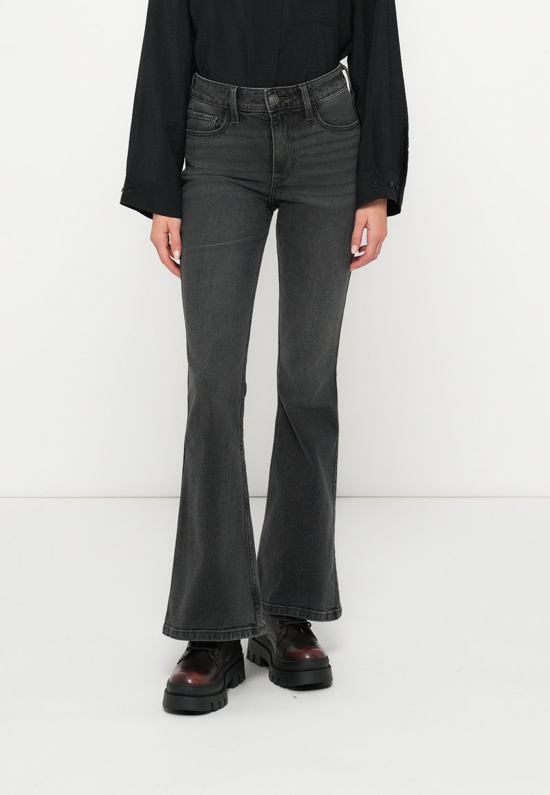 Platų juodų džinsų kelnės su aukštu juosmeniu, su subtiliomis dėvėjimo žymėmis, penkių kišenių dizainu ir kontrastingomis siūlėmis, derinamos su masyviomis platforminėmis botais.