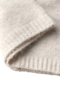 Manica di un maglione lavorato a maglia di colore beige chiaro con una consistenza morbida e pelosa e dettagli a costine al polsino. Il tessuto appare caldo e accogliente.