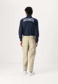 Tengerészeti pulcsi fehér "BARBOUR" felirattal a hátán, bézs cargo nadrággal, oldalzsebekkel és mandzsettákkal. Fehér sneakers.