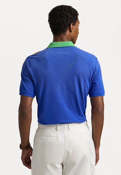 Camisa polo azul com colarinho verde, mangas curtas e um tecido texturizado. Apresenta um detalhe de design discreto no ombro.