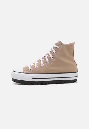 Beige højtop lærredsneakers med hvide snørebånd, hvid gummisål og sort slidbane, vist fra siden på en ensfarvet baggrund.