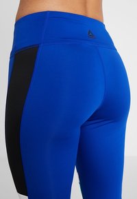 Blå träningsleggings med en svart sidopan, tillverkade av ett stretchtåligt material med en hög midja och slät yta.