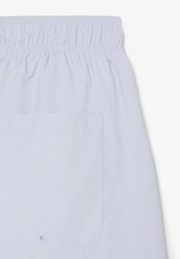 Shorts à taille élastique bleu clair avec une grande poche arrière unique dotée d'une petite fermeture à bouton au centre en bas.