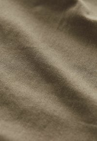 Baumwollstoff in einem sanften olivgrünen Farbton, mit feiner gerippter Textur, sanften, fließenden Falten und subtilen Farbvariationen.