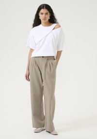 Vit oversized t-shirt med asymmetrisk halsringning, tillsammans med beige höga, vida byxor. Genomskinliga slip-on skor fulländar looken.