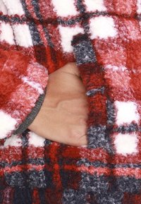 Rød og hvid ternet fleece-materiale med en blød tekstur. En hånd vises i en lomme, hvilket afslører en grå manchetdetalje.