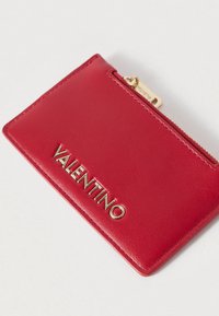 Δερμάτινη θήκη καρτών σε κόκκινο με ομαλή υφή, διαθέτει χρυσό λογότυπο "VALENTINO" και διαμερίσμα με φερμουάρ στο επάνω μέρος.