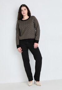 Pull noir à motifs avec un design géométrique, associé à un pantalon noir et des escarpins beiges à bout pointu. Le pull a un col rond et des poignets côtelés.