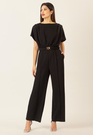 Schwarzer Jumpsuit mit weitem Beinanschnitt, kurzen Ärmeln, elastischem Bund und einem goldenen, runden Akzent an der Taille für zusätzlichen Flair.
