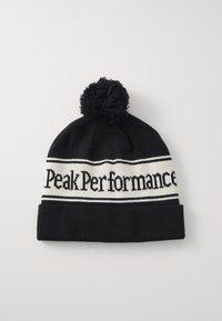 Černá pletená čepice s bílým pruhem s textem "Peak Performance". Má černý pom-pom nahoře a ohnutý lem.