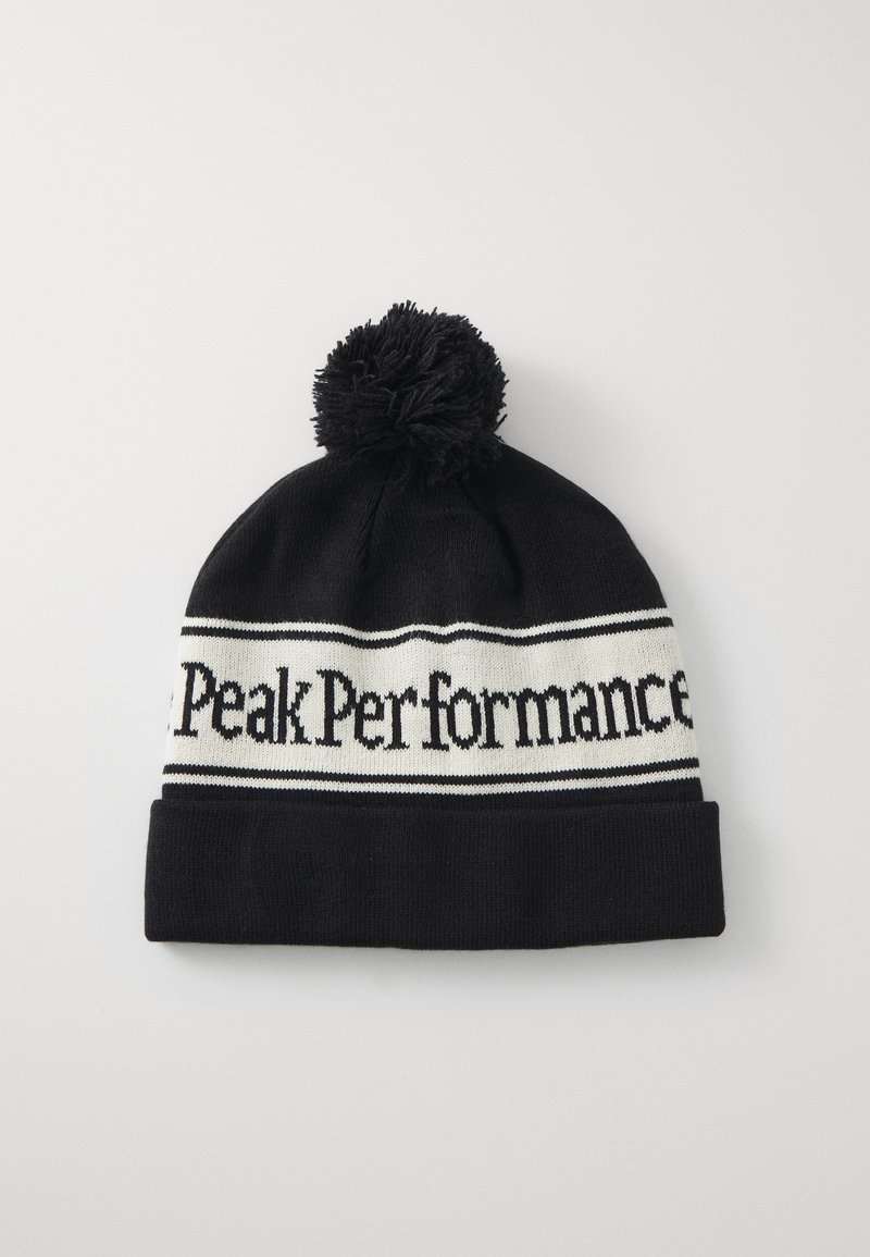 Černá pletená čepice s bílým pruhem s textem "Peak Performance". Má černý pom-pom nahoře a ohnutý lem.