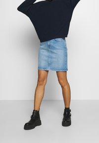 Jeansrock in Hellblau, knielang mit schmaler Silhouette. Kombiniert mit schwarzen Knöchelstiefeln, die eine dicke Sohle und eine Schnallenverzierung aufweisen.