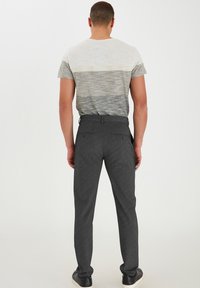 Pantalones grises texturizados y una camisa de manga corta a rayas, vista desde atrás. La camisa tiene colores en gradiente horizontal en gris y crema.